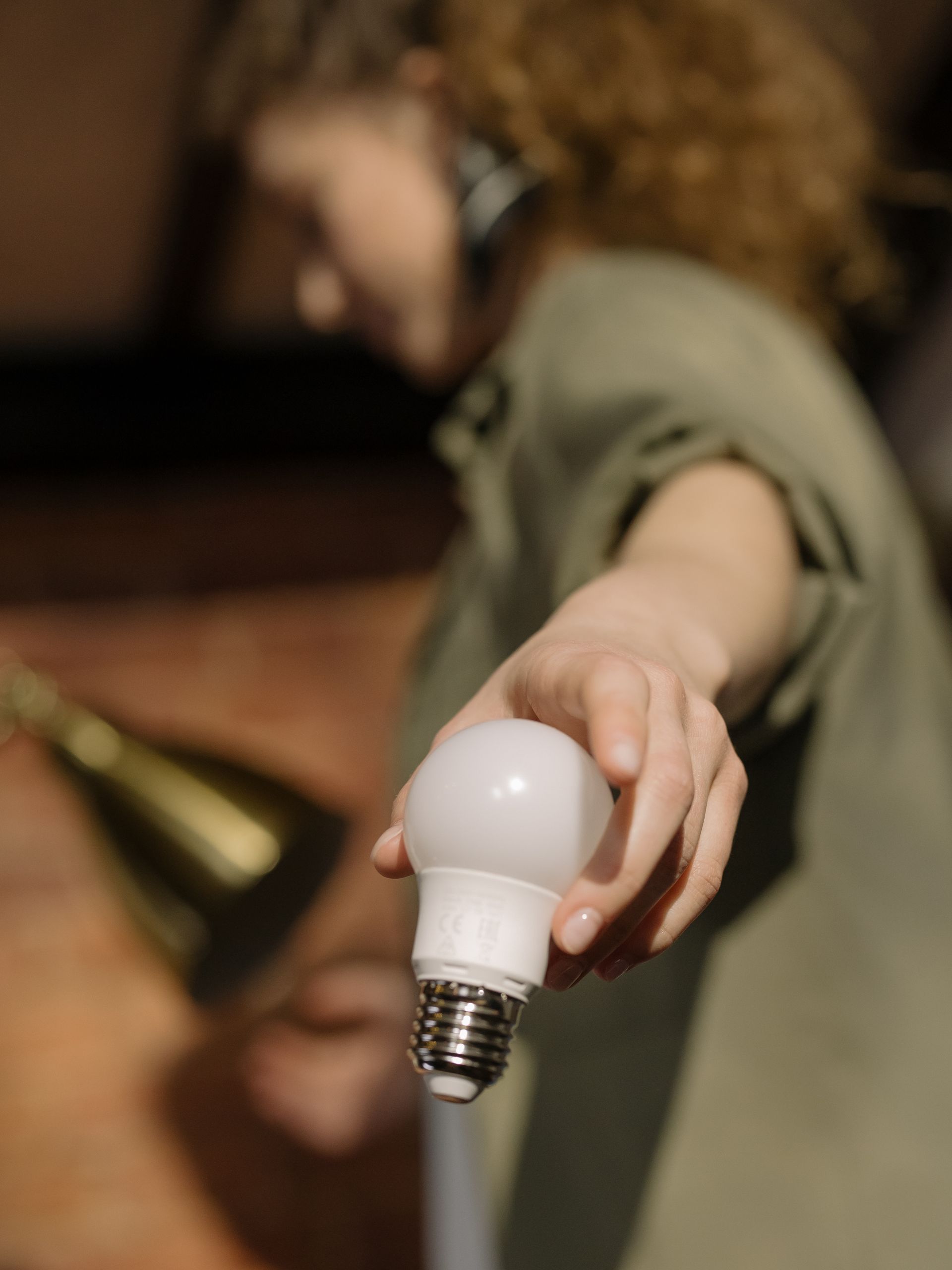 A woman changes a light bulb indoors, emphasizing home maintenance.