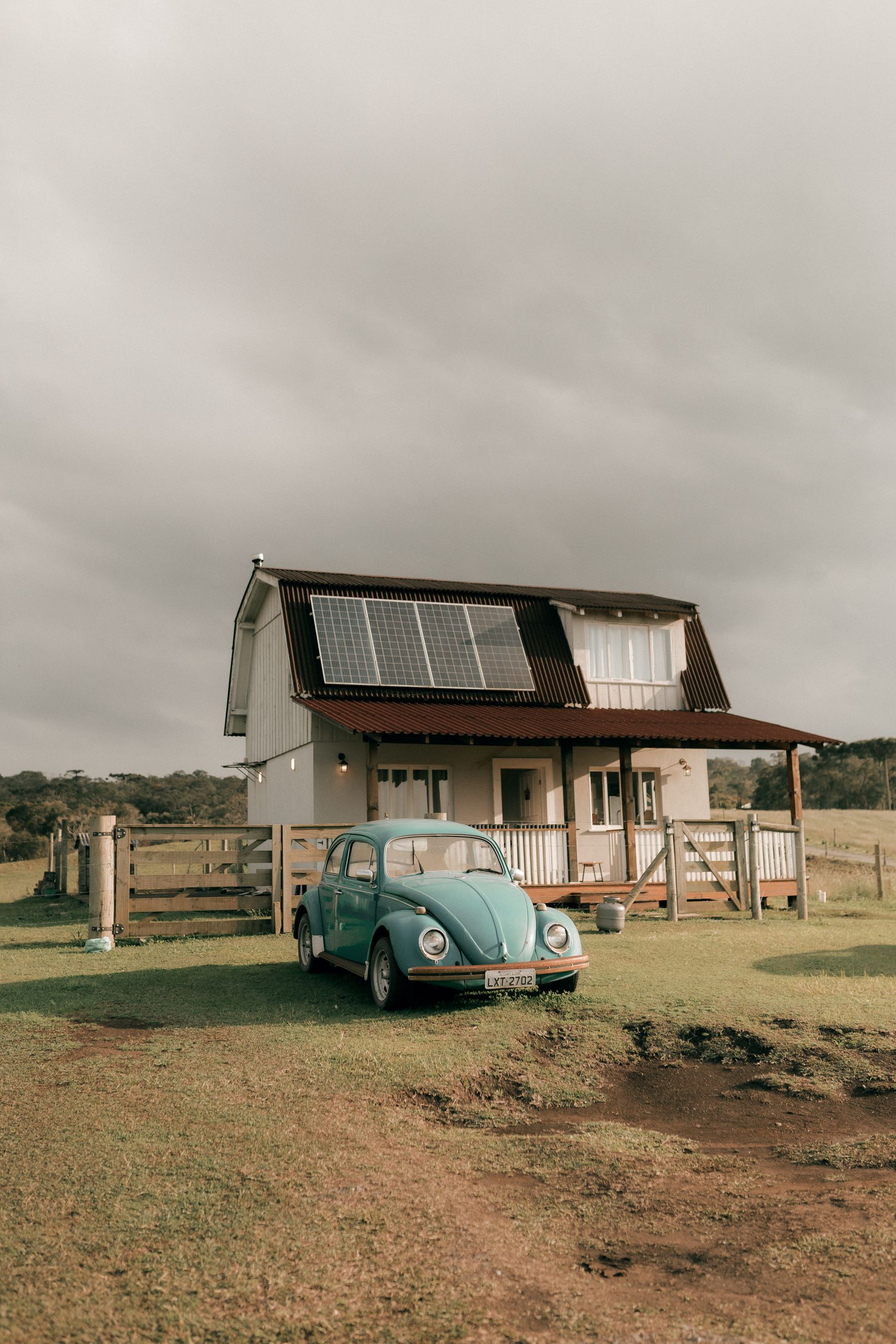 Charming rural scene with a farmhouse, vintage car, and solar panels under a cloudy sky.