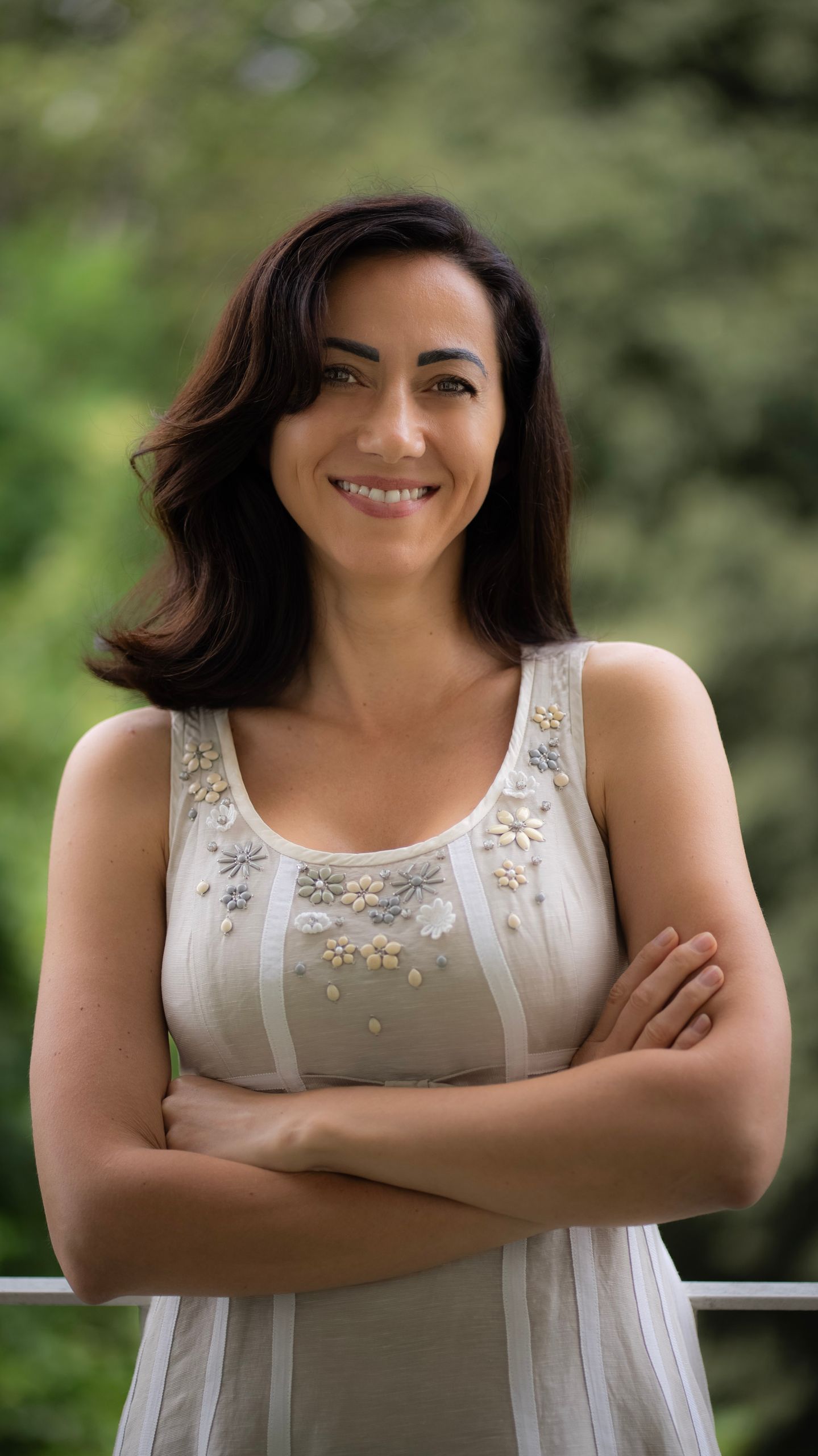 Elegant woman smiling with arms crossed in a serene outdoor setting in Milan, Italy.